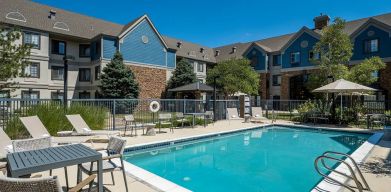 The hotel’s outdoor pool features tables and chairs, with shade available, and sun loungers by the side, with greenery beyond the fence.