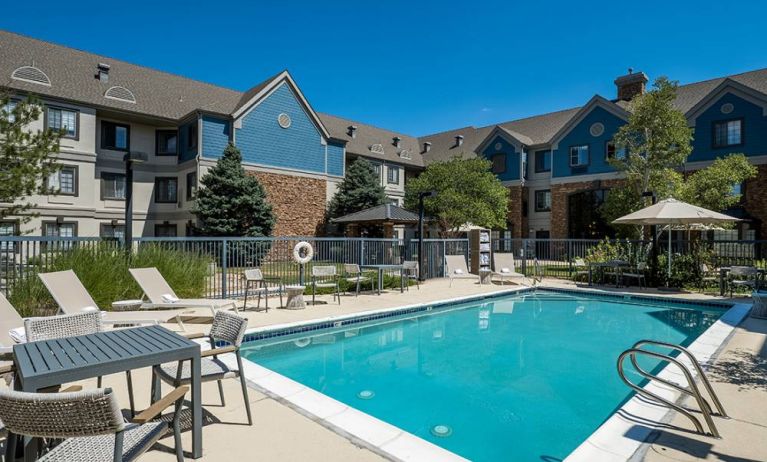 The hotel’s outdoor pool features tables and chairs, with shade available, and sun loungers by the side, with greenery beyond the fence.