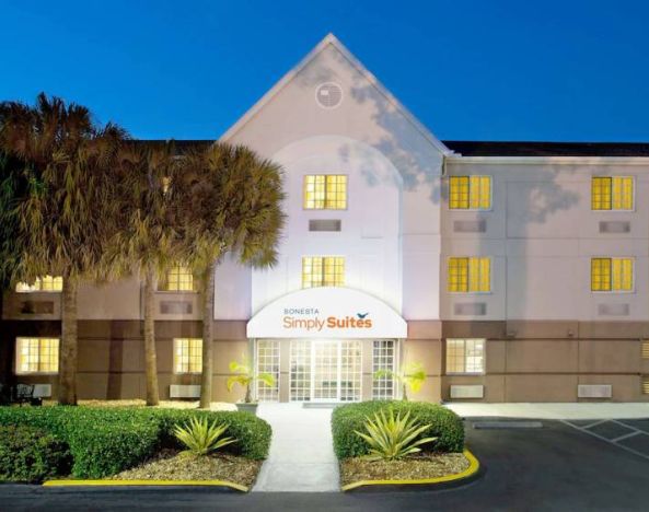 The hotel’s exterior has the name Sonesta Simply Suites above the front door, with parking spaces and foliage including trees nearby.