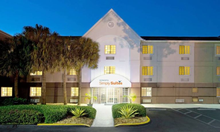 The hotel’s exterior has the name Sonesta Simply Suites above the front door, with parking spaces and foliage including trees nearby.