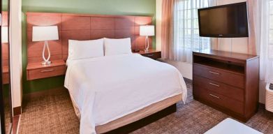 Double bed guest room in Sonesta ES Suites Fort Lauderdale Plantation, featuring bedside lamps, windows, and a large TV.