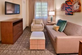 Sonesta ES Suites Fort Lauderdale Plantation guest room living area, furnished with sofa, armchair, window, and a widescreen television.