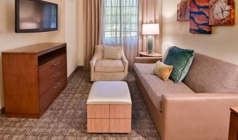 Sonesta ES Suites Fort Lauderdale Plantation guest room living area, furnished with sofa, armchair, window, and a widescreen television.