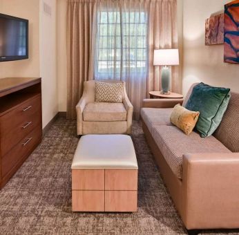 Sonesta ES Suites Fort Lauderdale Plantation guest room living area, furnished with sofa, armchair, window, and a widescreen television.