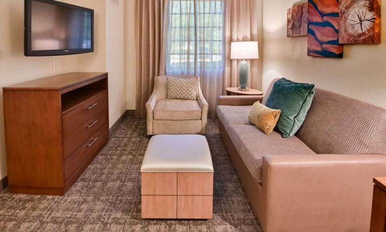 Sonesta ES Suites Fort Lauderdale Plantation guest room living area, furnished with sofa, armchair, window, and a widescreen television.