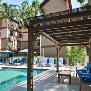 Sonesta ES Suites Fort Lauderdale Plantation’s outdoor pool has sofa seating and a coffee table by the side, alongside a row of sun loungers.