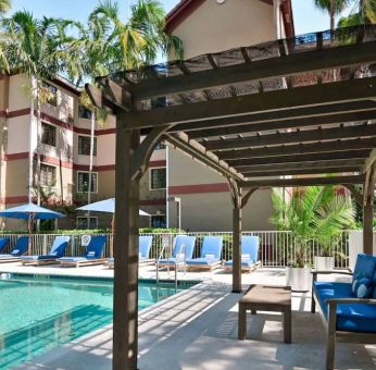 Sonesta ES Suites Fort Lauderdale Plantation’s outdoor pool has sofa seating and a coffee table by the side, alongside a row of sun loungers.