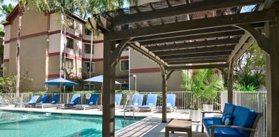 Sonesta ES Suites Fort Lauderdale Plantation’s outdoor pool has sofa seating and a coffee table by the side, alongside a row of sun loungers.