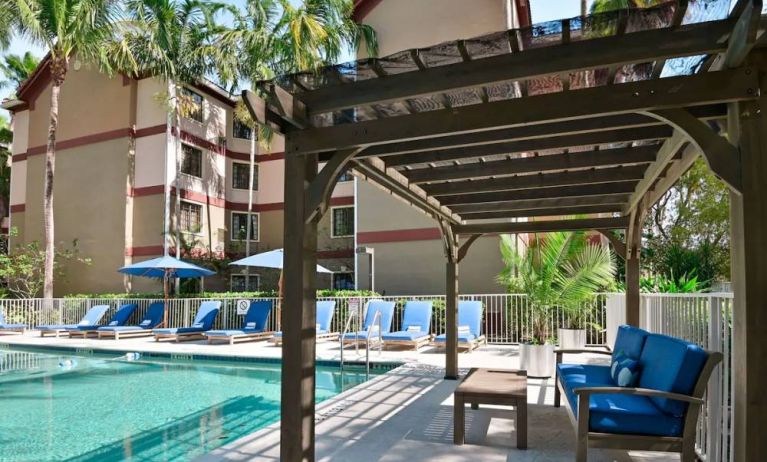 Sonesta ES Suites Fort Lauderdale Plantation’s outdoor pool has sofa seating and a coffee table by the side, alongside a row of sun loungers.