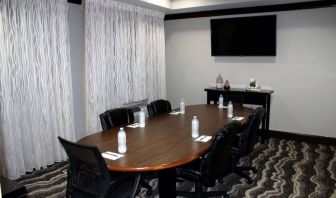 Hotel meeting room, including a wooden table and five leather chairs around it, two windows, and a large TV on the wall.