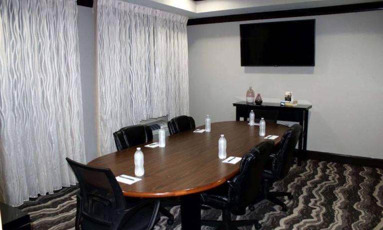 Hotel meeting room, including a wooden table and five leather chairs around it, two windows, and a large TV on the wall.