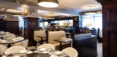 The hotel’s restaurant offers both table and booth seating, with a mix of white seats and dark wood tables, plus a bar.