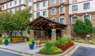 The hotel’s exterior has a pair of benches beside the covered entrance, with flowerbeds, bushes, and trees nearby.