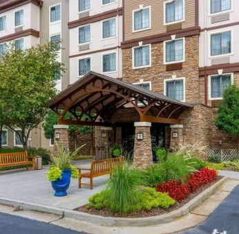 The hotel’s exterior has a pair of benches beside the covered entrance, with flowerbeds, bushes, and trees nearby.