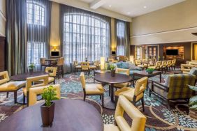 The hotel’s breakfast area has a carpeted floor, range of table sizes, seating from normal chairs to tall stools and armchairs, high ceilings and large windows, plus multiple TVs.