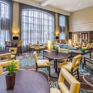 The hotel’s breakfast area has a carpeted floor, range of table sizes, seating from normal chairs to tall stools and armchairs, high ceilings and large windows, plus multiple TVs.