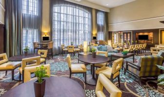 The hotel’s breakfast area has a carpeted floor, range of table sizes, seating from normal chairs to tall stools and armchairs, high ceilings and large windows, plus multiple TVs.