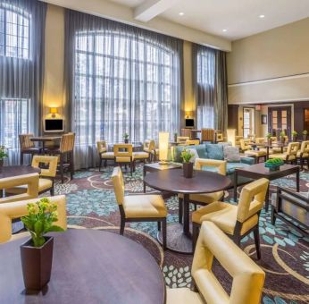 The hotel’s breakfast area has a carpeted floor, range of table sizes, seating from normal chairs to tall stools and armchairs, high ceilings and large windows, plus multiple TVs.