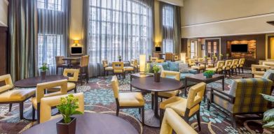 The hotel’s breakfast area has a carpeted floor, range of table sizes, seating from normal chairs to tall stools and armchairs, high ceilings and large windows, plus multiple TVs.