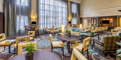 The hotel’s breakfast area has a carpeted floor, range of table sizes, seating from normal chairs to tall stools and armchairs, high ceilings and large windows, plus multiple TVs.