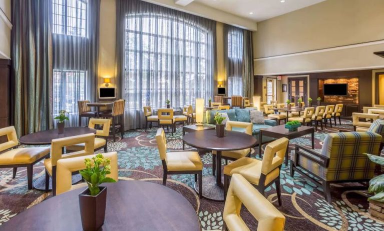 The hotel’s breakfast area has a carpeted floor, range of table sizes, seating from normal chairs to tall stools and armchairs, high ceilings and large windows, plus multiple TVs.