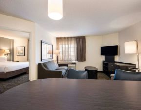 Sonesta Simply Suites Detroit Troy double bed guest room, including living area with table and chairs, sofa, TV, and window.