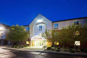 The hotel’s exterior has potted plants and benches by the front door, with trees and bushes nearby.