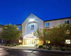 The hotel’s exterior has potted plants and benches by the front door, with trees and bushes nearby.