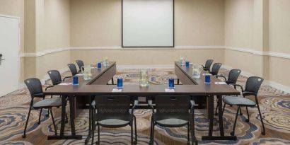 Meeting room in Sonesta White Plains Downtown, with tables arranged in a U-shape, seating for 10, and a projector screen.