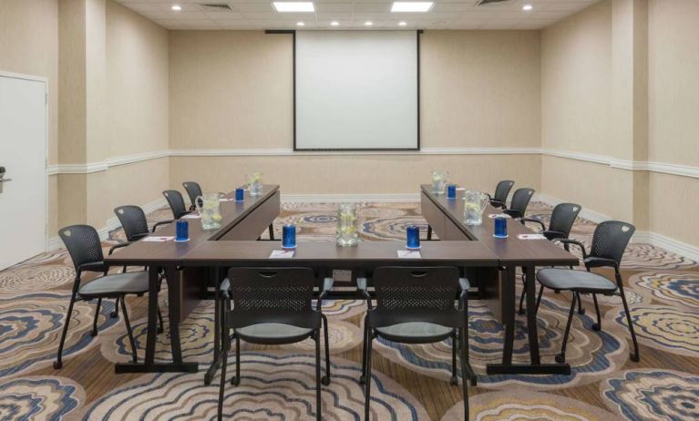 Meeting room in Sonesta White Plains Downtown, with tables arranged in a U-shape, seating for 10, and a projector screen.