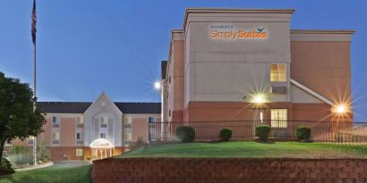 Sonesta Simply Suites Oklahoma City Airport’s exterior has a USA flag, abundant greenery including well-trimmed bushes, and the hotel chain’s name clearly indicated.