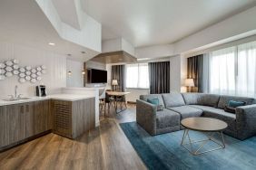 Guest room living area in Sonesta Columbus Downtown, including corner sofa and coffee table, large windows, and a TV with table and chairs nearby.