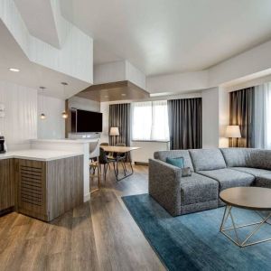 Guest room living area in Sonesta Columbus Downtown, including corner sofa and coffee table, large windows, and a TV with table and chairs nearby.