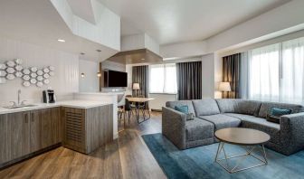 Guest room living area in Sonesta Columbus Downtown, including corner sofa and coffee table, large windows, and a TV with table and chairs nearby.