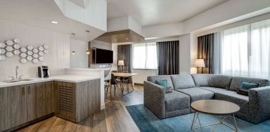 Guest room living area in Sonesta Columbus Downtown, including corner sofa and coffee table, large windows, and a TV with table and chairs nearby.