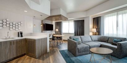 Guest room living area in Sonesta Columbus Downtown, including corner sofa and coffee table, large windows, and a TV with table and chairs nearby.