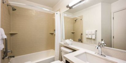 Guest bathroom in Sonesta Simply Suites Austin South, featuring mirror, sink, and lavatory, plus a bath equipped with a shower.