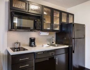 Sonesta Simply Suites Austin The Domain Area guest room kitchen, with fridge-freezer, sink, microwave, and hob.