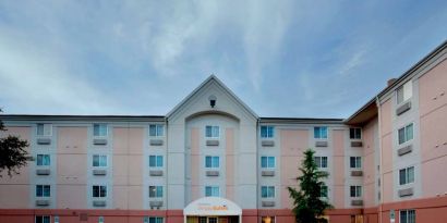 The hotel’s exterior includes disabled parking spaces close to the front door, potted plants, and a tall tree.