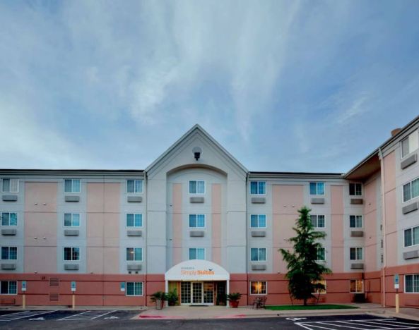 The hotel’s exterior includes disabled parking spaces close to the front door, potted plants, and a tall tree.