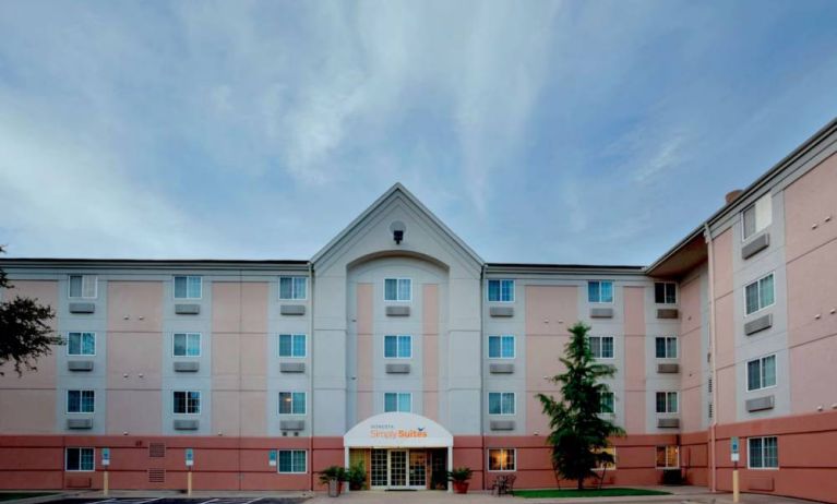 The hotel’s exterior includes disabled parking spaces close to the front door, potted plants, and a tall tree.