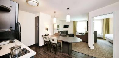 Sonesta Simply Suites Houston CityCentre I-10 West guest room, featuring a kitchen and lounge area, between which is a table and three chairs.