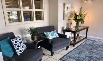 The hotel lobby is furnished with a pair of armchairs, a coffee table, art on the wall, and potted plants.