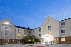 The hotel’s exterior includes parking close to the front door, benches, potted plants, plus bushes, trees, and flowers.