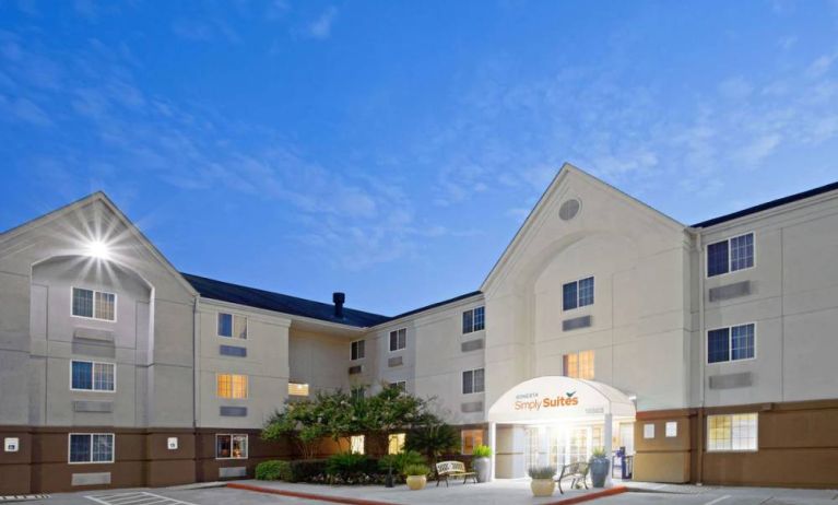 The hotel’s exterior includes parking close to the front door, benches, potted plants, plus bushes, trees, and flowers.