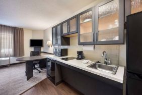 Sonesta Simply Suites Plano Frisco’s kitchen features a table and chair, microwave, hob, and fridge-freezer.