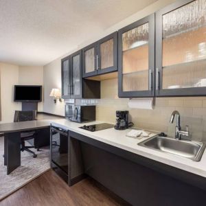 Sonesta Simply Suites Plano Frisco’s kitchen features a table and chair, microwave, hob, and fridge-freezer.