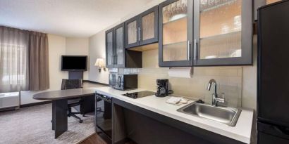 Sonesta Simply Suites Plano Frisco’s kitchen features a table and chair, microwave, hob, and fridge-freezer.