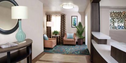 Sonesta Simply Suites Plano Frisco’s lobby features a pair of armchairs, window, coffee table, and potted plants.