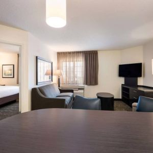 Sonesta Simply Suites Dallas Las Colinas double bed guest room, including sofa, window, and TV.